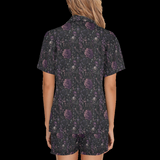 Back view of woman wearing black night floral short pajamas with purple skull-and-flower print on a black background
