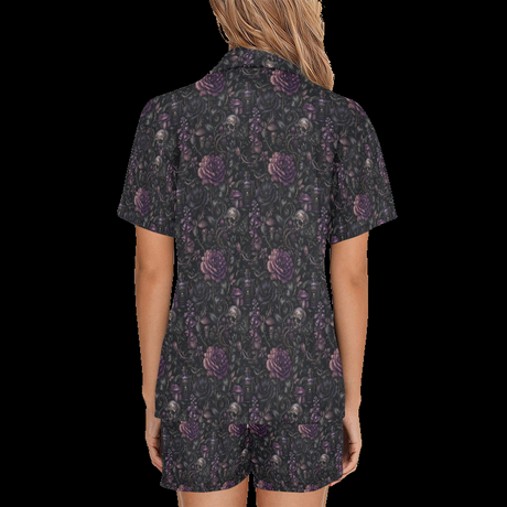 Back view of woman wearing black night floral short pajamas with purple skull-and-flower print on a black background